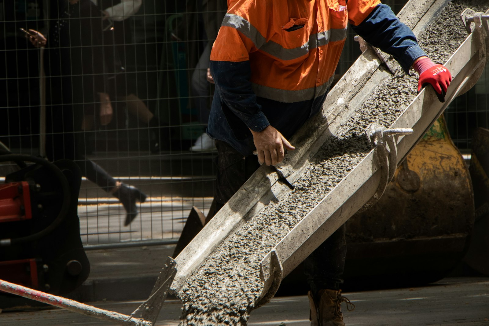 Concrete worker in hi-vis guiding wet concrete down a mixer truck chute on a job site