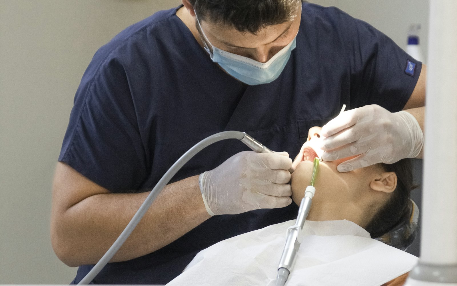 Dentist in navy scrubs and a mask treating a patient reclined in the chair