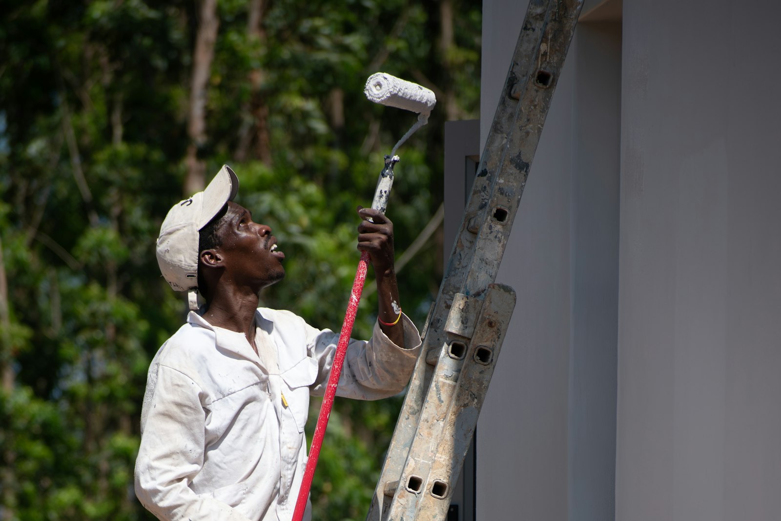 House painter on a ladder rolling fresh paint onto an exterior wall
